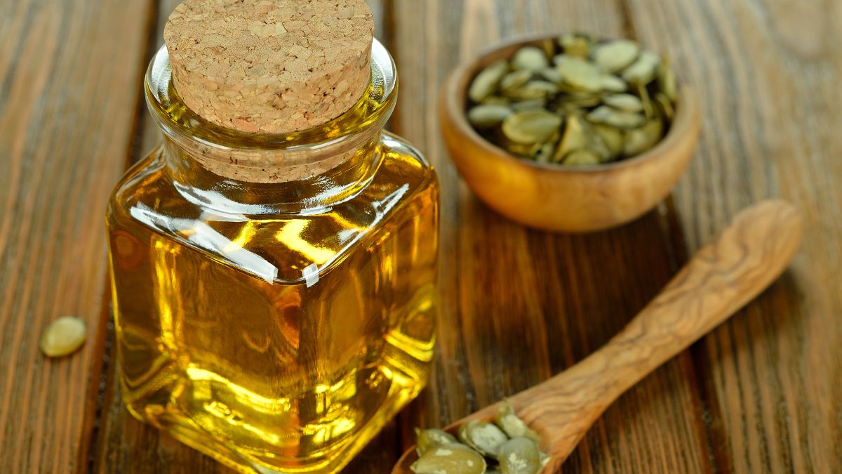 Egy üveg tökmagolaj, mellette tökmagok egy tálban és kanálban.