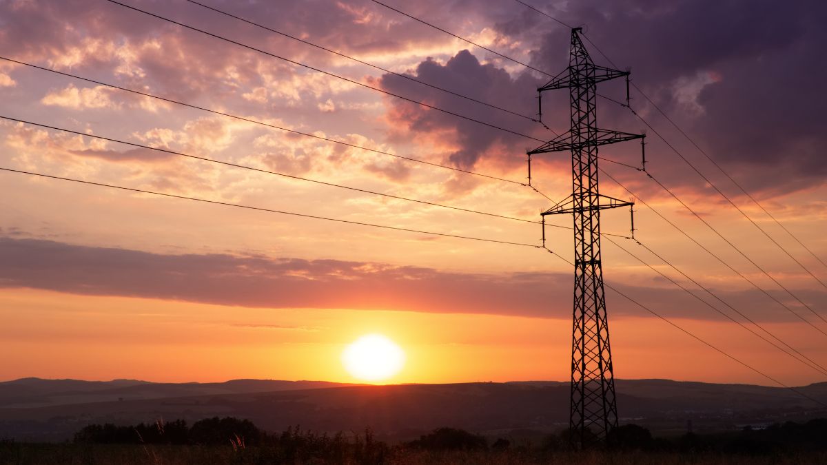 Egy magas feszültségű villanyoszlop a naplementében, elektromos vezetékekkel.