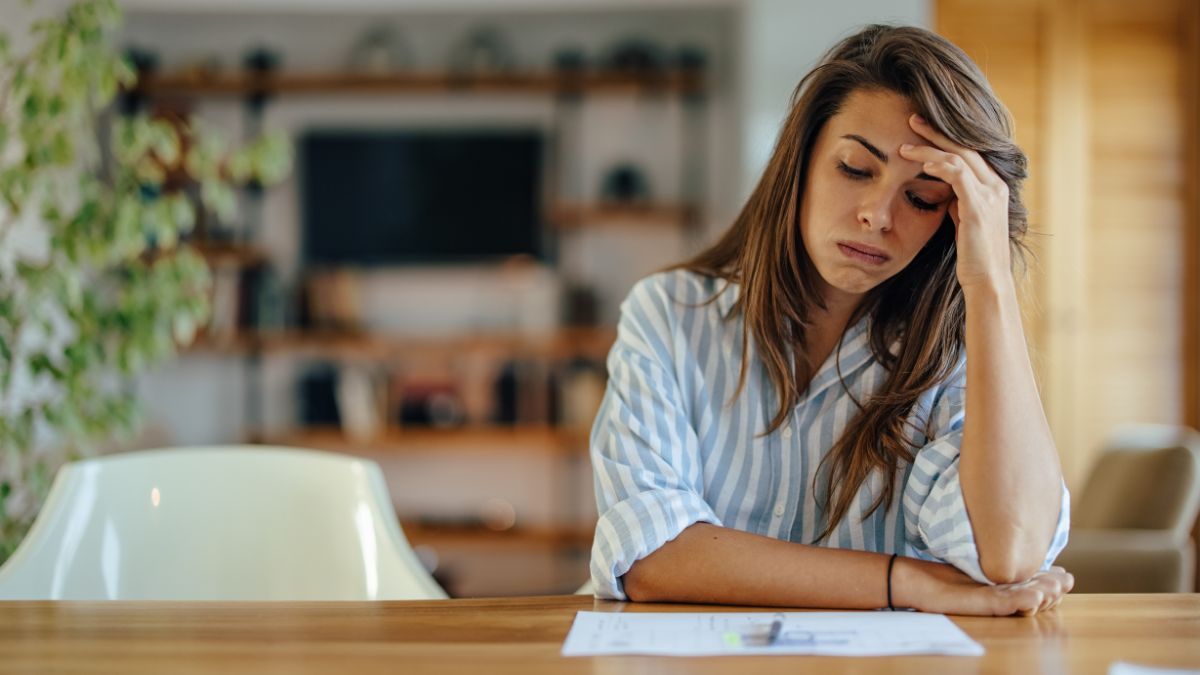 Túlgondolsz mindent? 5 mentális technika, amivel lecsendesítheted a zakatoló elméd 9 Egy fiatal nő gondterhelten ül egy asztalnál, papírok előtt.