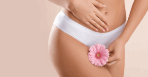 Egy női kéz egy virágot tart az intim területen, fehér alsóneműben.