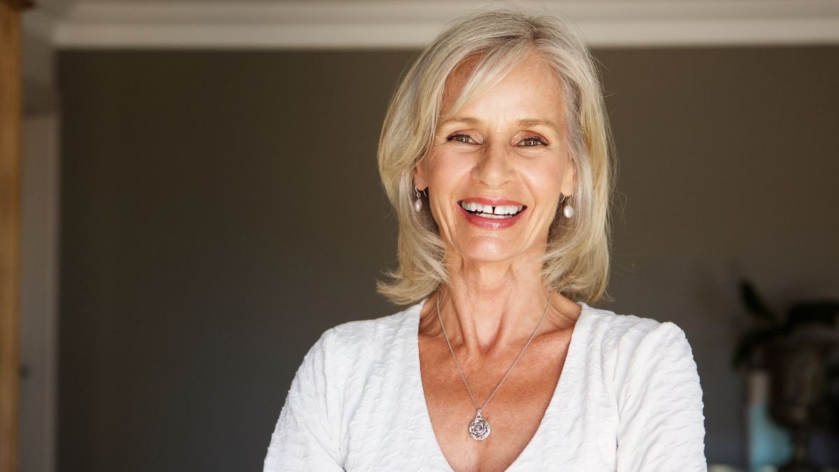 Vagány frizurák 50 felett 3 Egy mosolygó nő, aki 50 felett van, modern frizurával és elegáns ruhában.