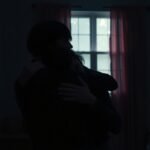 Pár intim ölelkezik a sötét szobában, érzelmi kapcsolódás tükrözve.