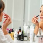 Nő sminkelés közben bőrápolási termékekkel egy tükör előtt.